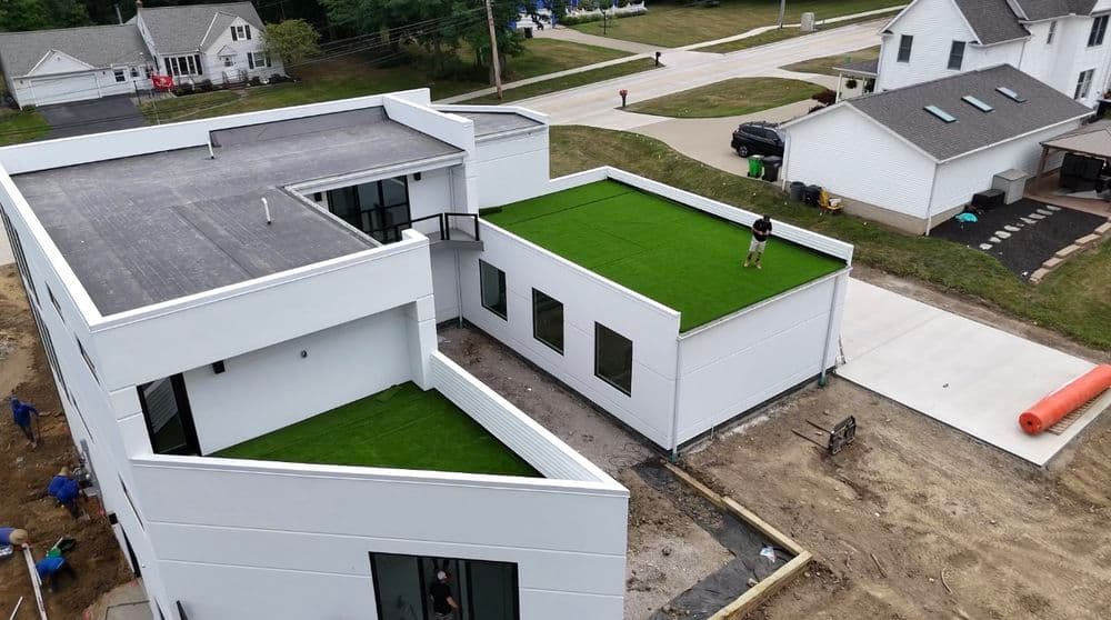 Modern white house with green rooftops and construction workers outdoors.