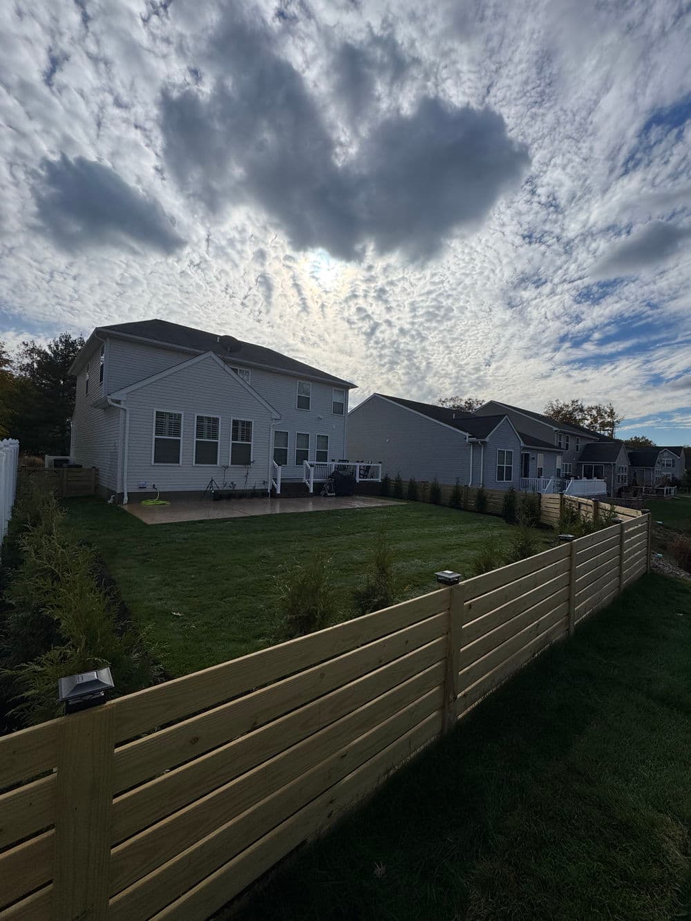 Modern backyard with lush grass, wooden fence, and cloudy sky in a suburban neighborhood.
