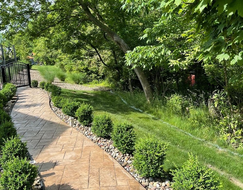 Scenic garden pathway with stamped concrete, lush greenery, and decorative shrubs.