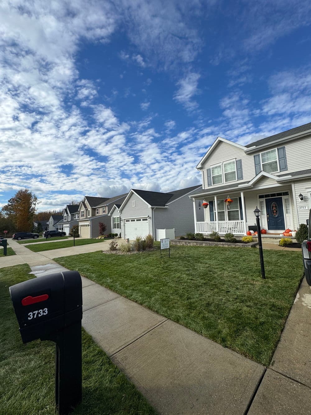 Residential neighborhood with a gray house, mailbox, and clear blue sky.