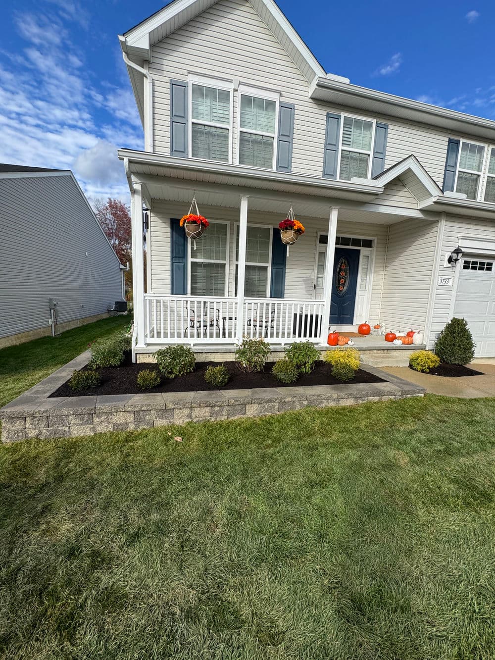 Front porch of a modern house with pumpkins, flowers, and landscaped garden in autumn.
