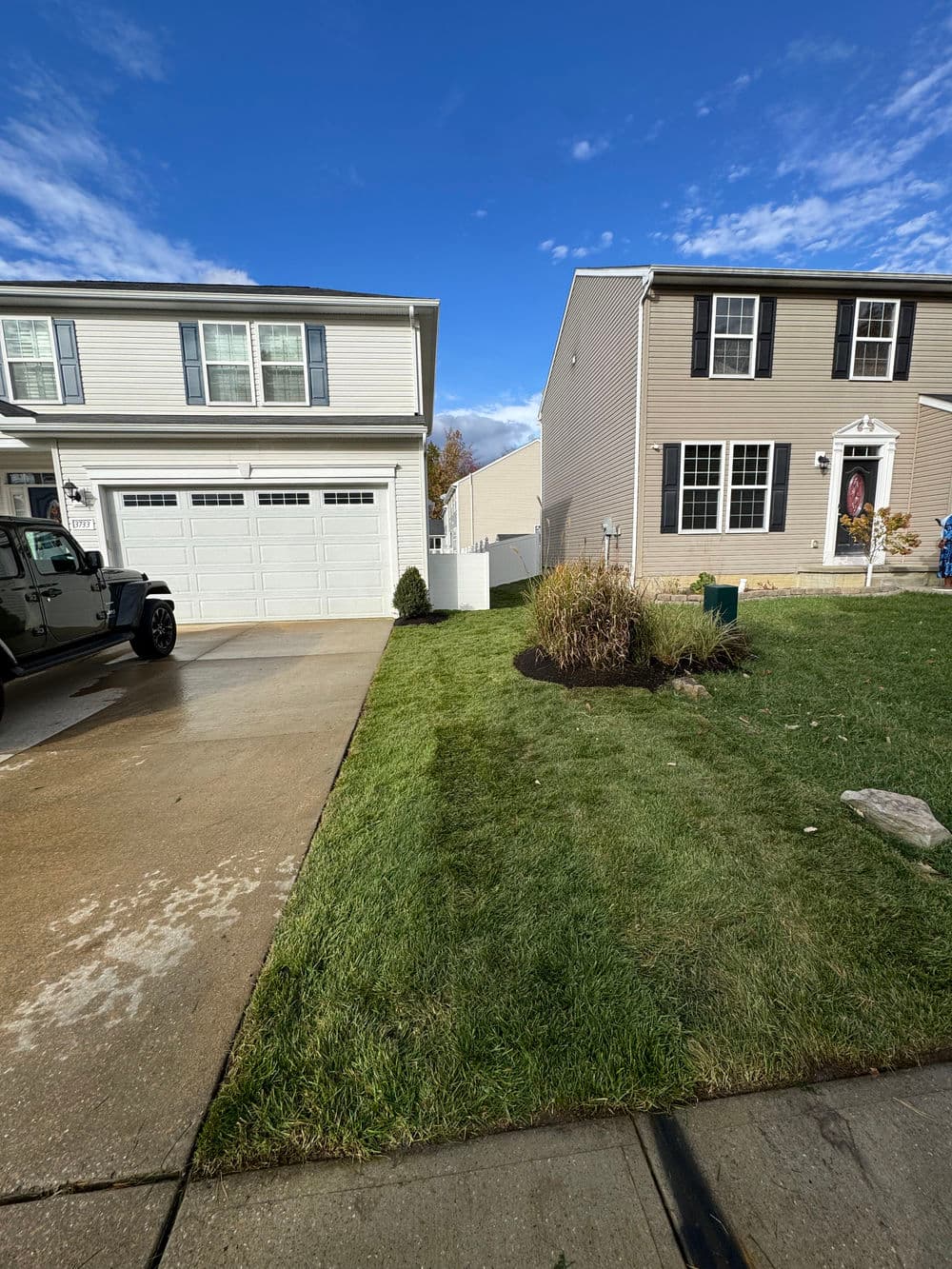 Driveway with two homes, freshly cut grass, and clear blue sky. Ideal suburban landscape.