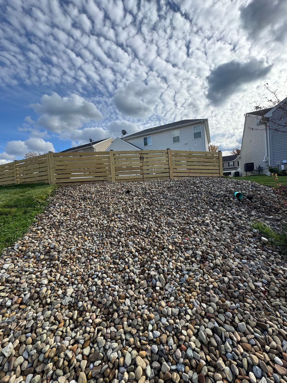 Gravel landscape with wooden fence and cloudy sky in a residential area.