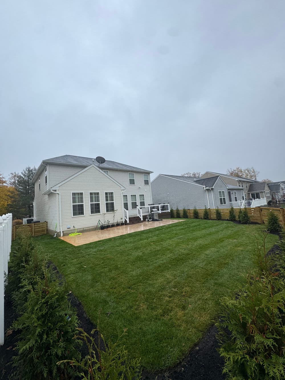 Rainy day landscape featuring a residential backyard with green grass and nearby homes.