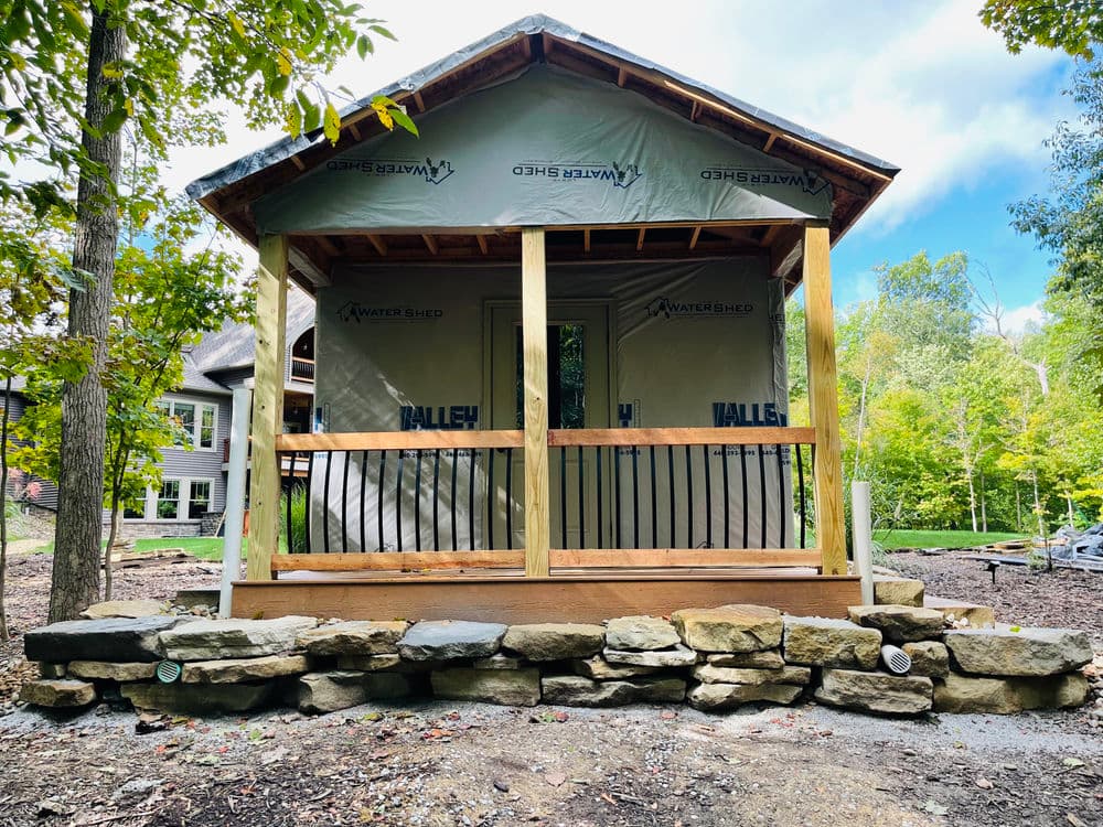 Newly constructed cabin porch with stone foundation and natural surroundings.