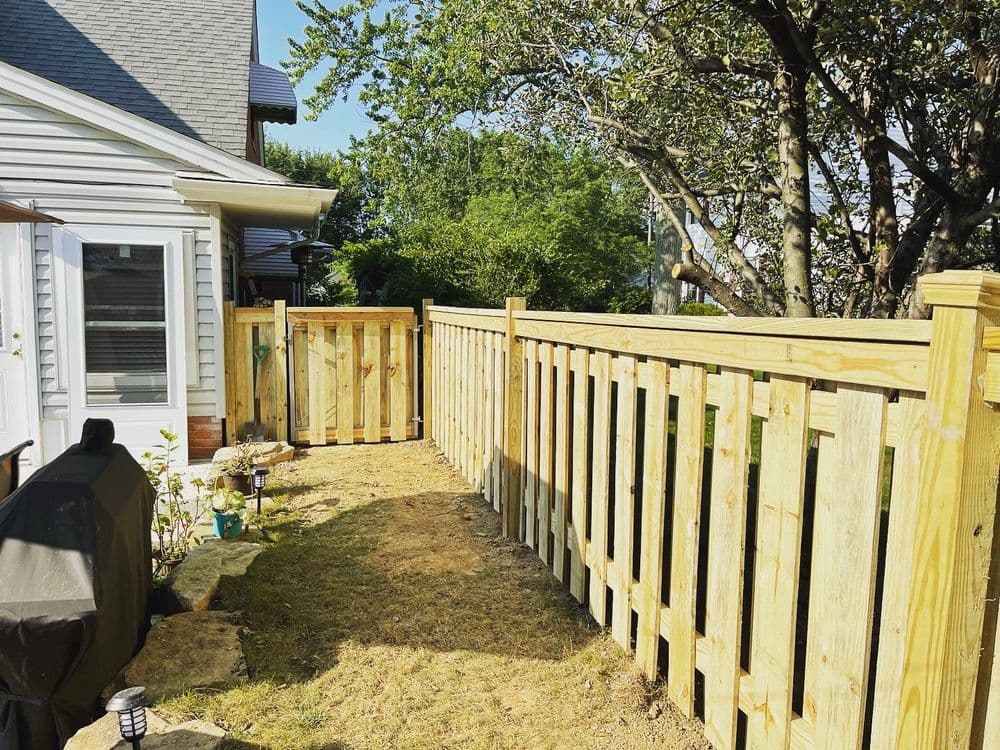 Wooden fence enclosing a backyard pathway with landscaping and outdoor furniture.