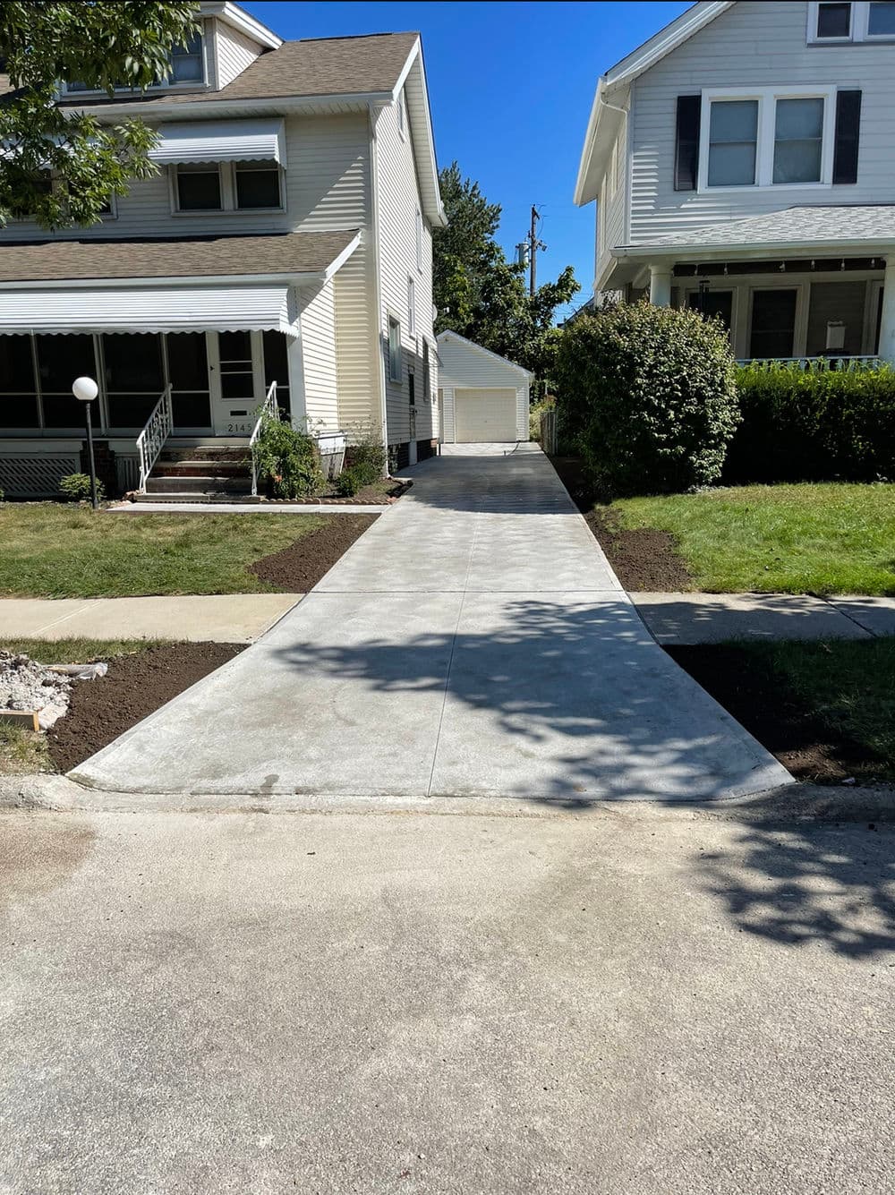 Newly paved concrete driveway extending between two houses, featuring landscaped edges.