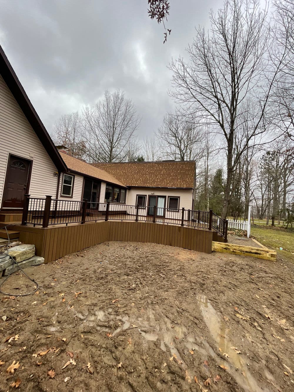 Newly built wooden deck extending from a house in a wooded area under a cloudy sky.