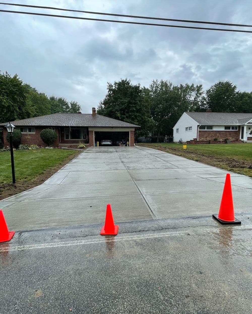 Freshly poured concrete driveway with orange traffic cones on a residential street.