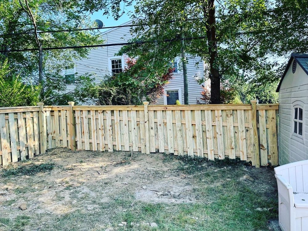 New wooden fence enclosing a backyard with a playhouse and trees in the background.