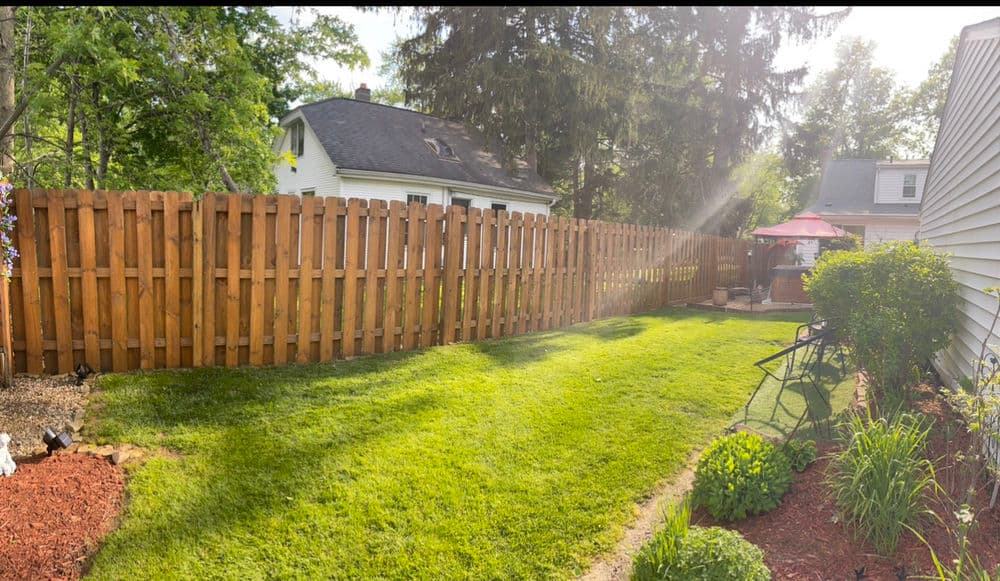 Lush backyard with wooden fence, green lawn, and sunlit patio area. Ideal for outdoor relaxation.
