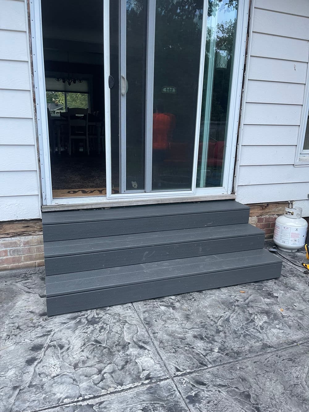 Gray wooden steps leading to a sliding glass door at a home entrance.