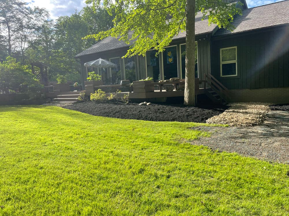Lush green lawn and landscaped yard leading to a wooden porch of a modern black house.