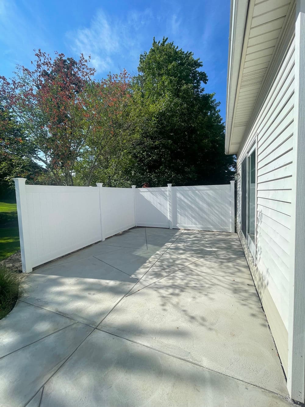 Sunny outdoor patio with a white fence and green trees in the background.