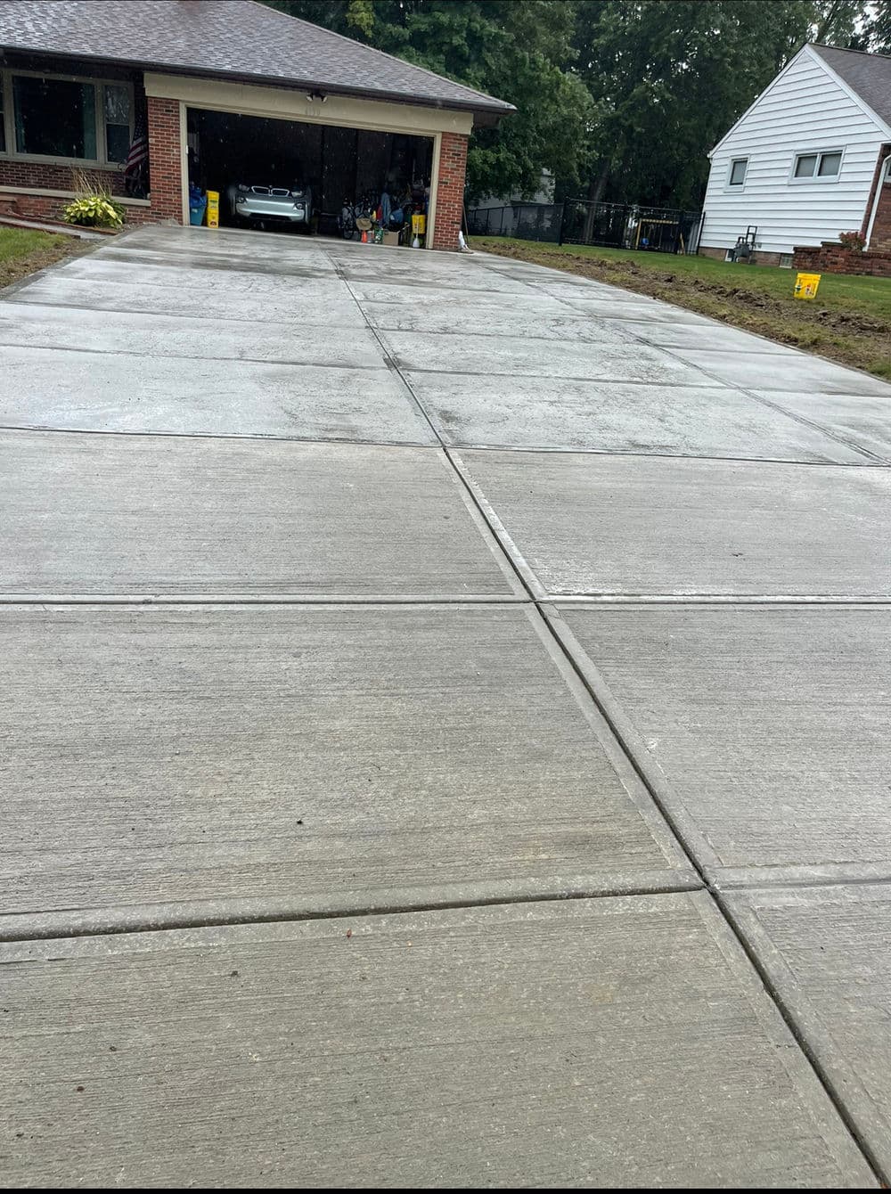 Newly poured concrete driveway in front of a suburban home with a parked car in the garage.