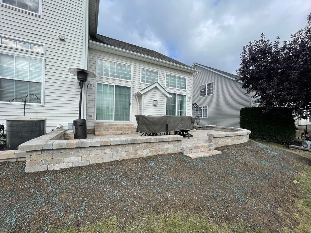 Patio area with stonework and outdoor furniture cover beside a house under cloudy sky.