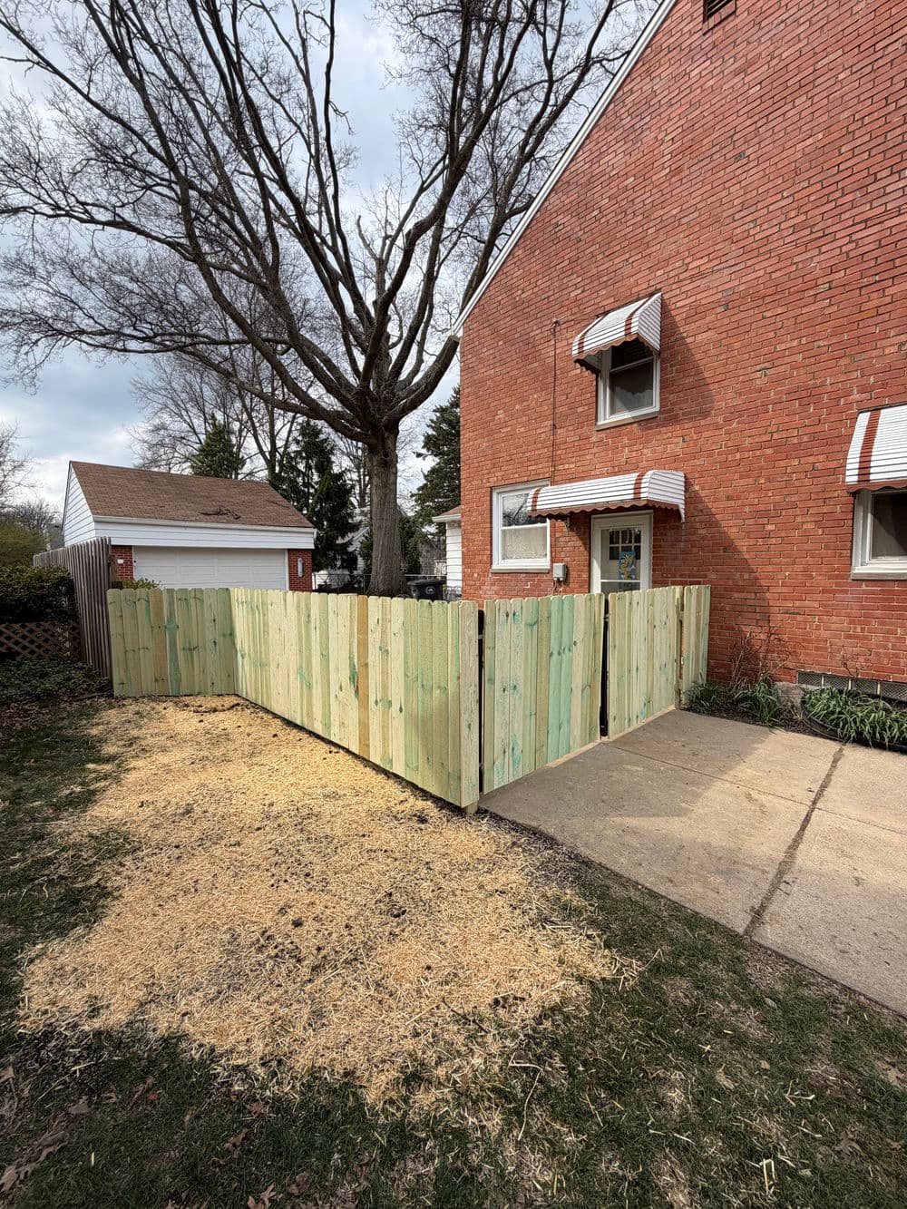 New wooden fence installation around yard, featuring green planks, near brick house and garage.