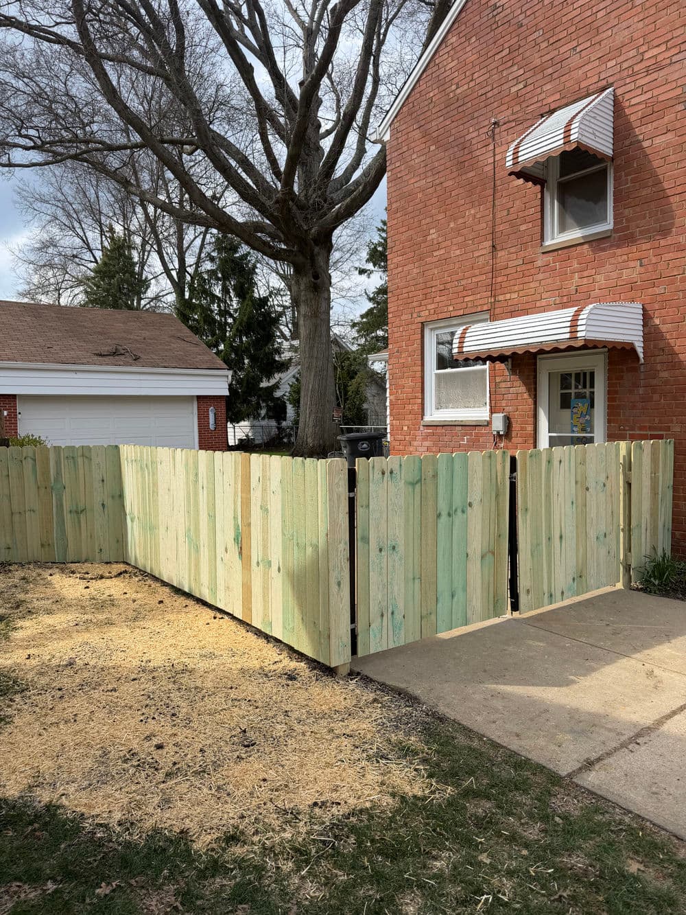 New wooden fence installation in front yard with a brick house and tree backdrop.