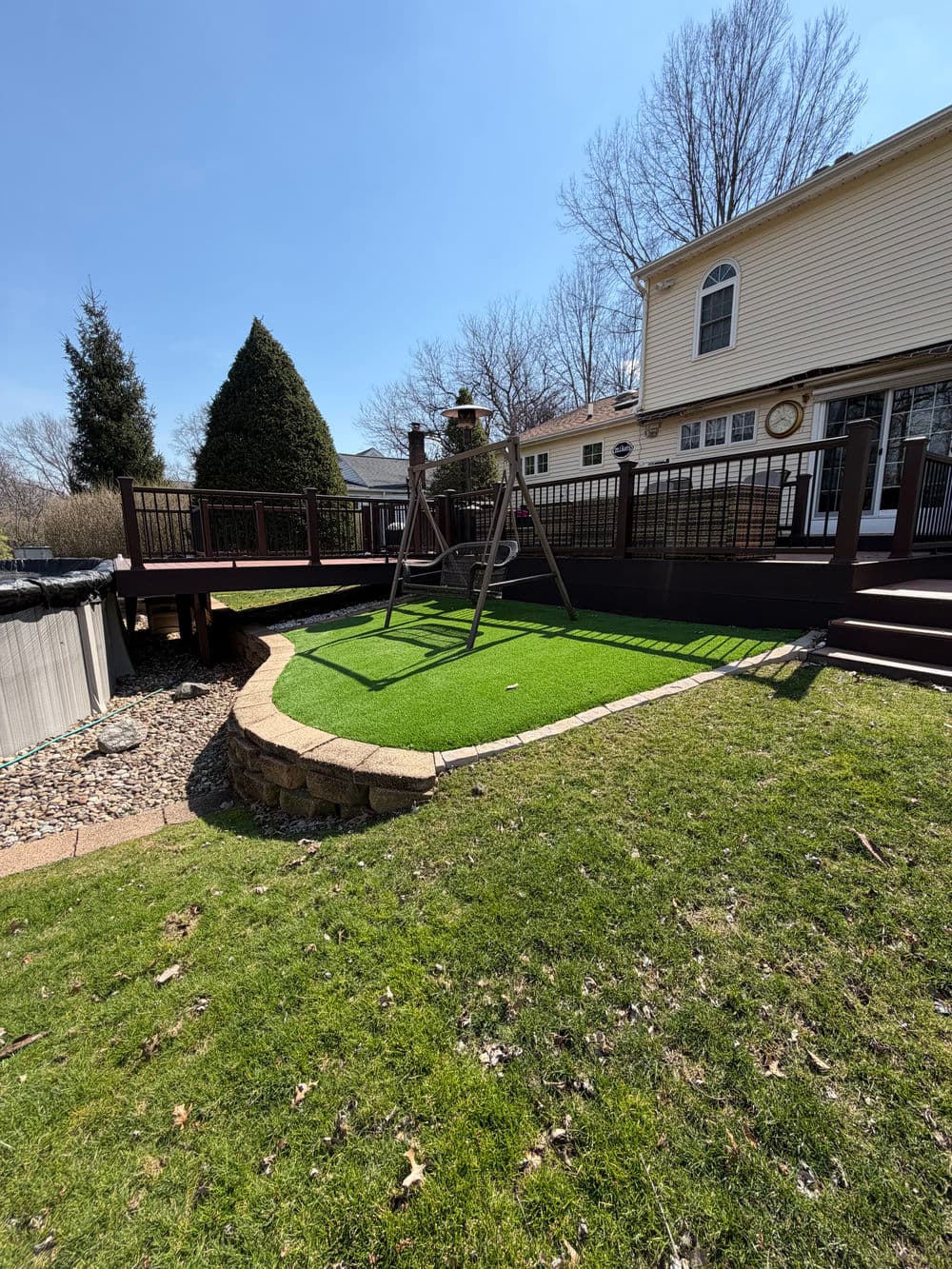 Backyard with artificial grass, wooden swingset, and deck under clear blue sky.