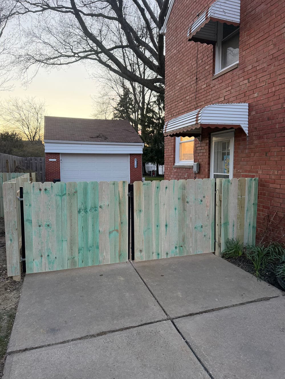 Wooden fence with a rustic finish, securing a driveway beside a red brick house and garage.