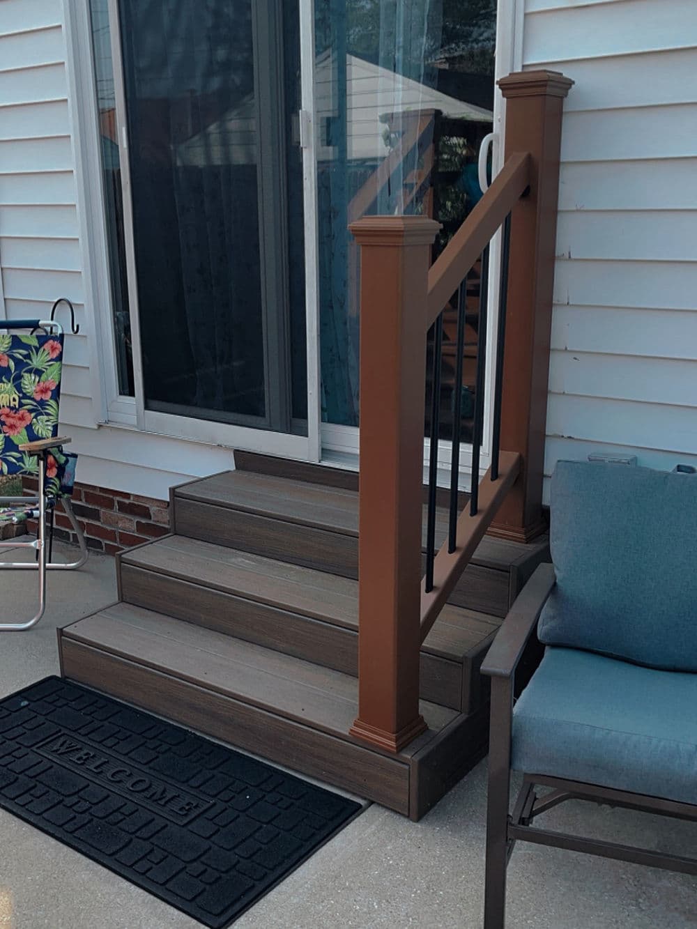 Composite stairs with a brown railing, leading to a sliding door, featuring a welcome mat.