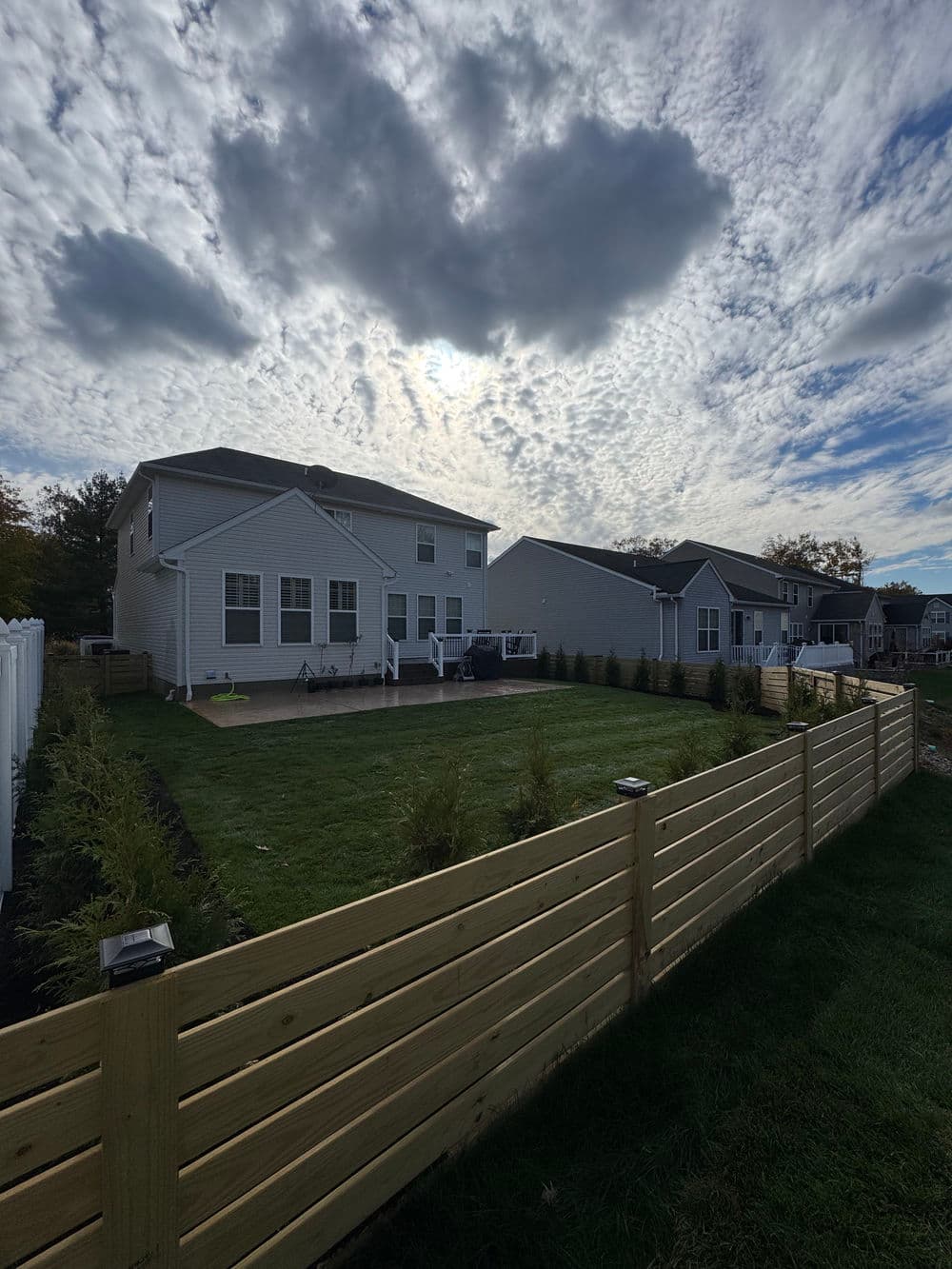 Modern backyard with a wooden fence, grassy area, and cloudy sky overhead.