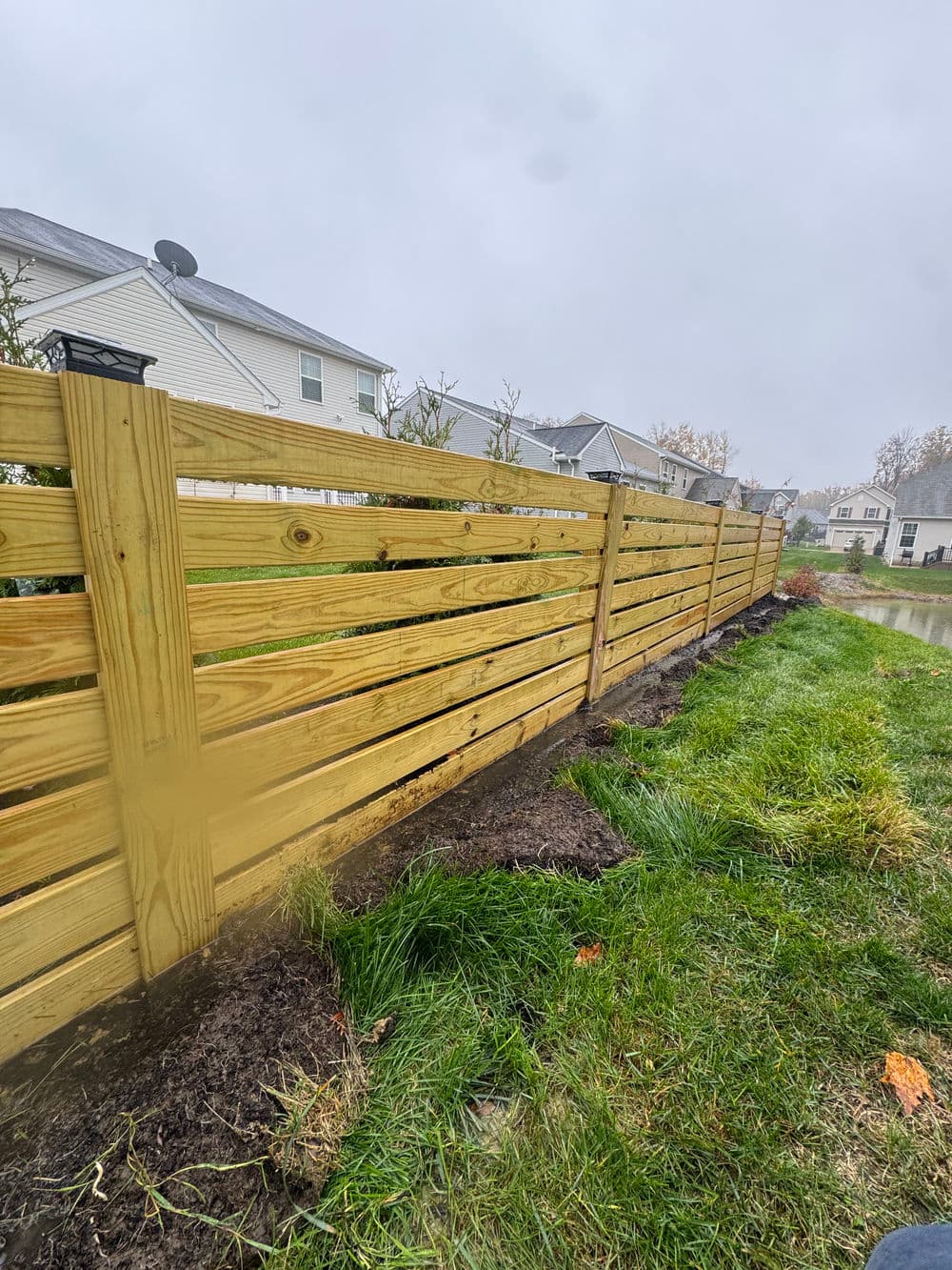 Wooden fence installation alongside a well-maintained grassy area in a residential neighborhood.