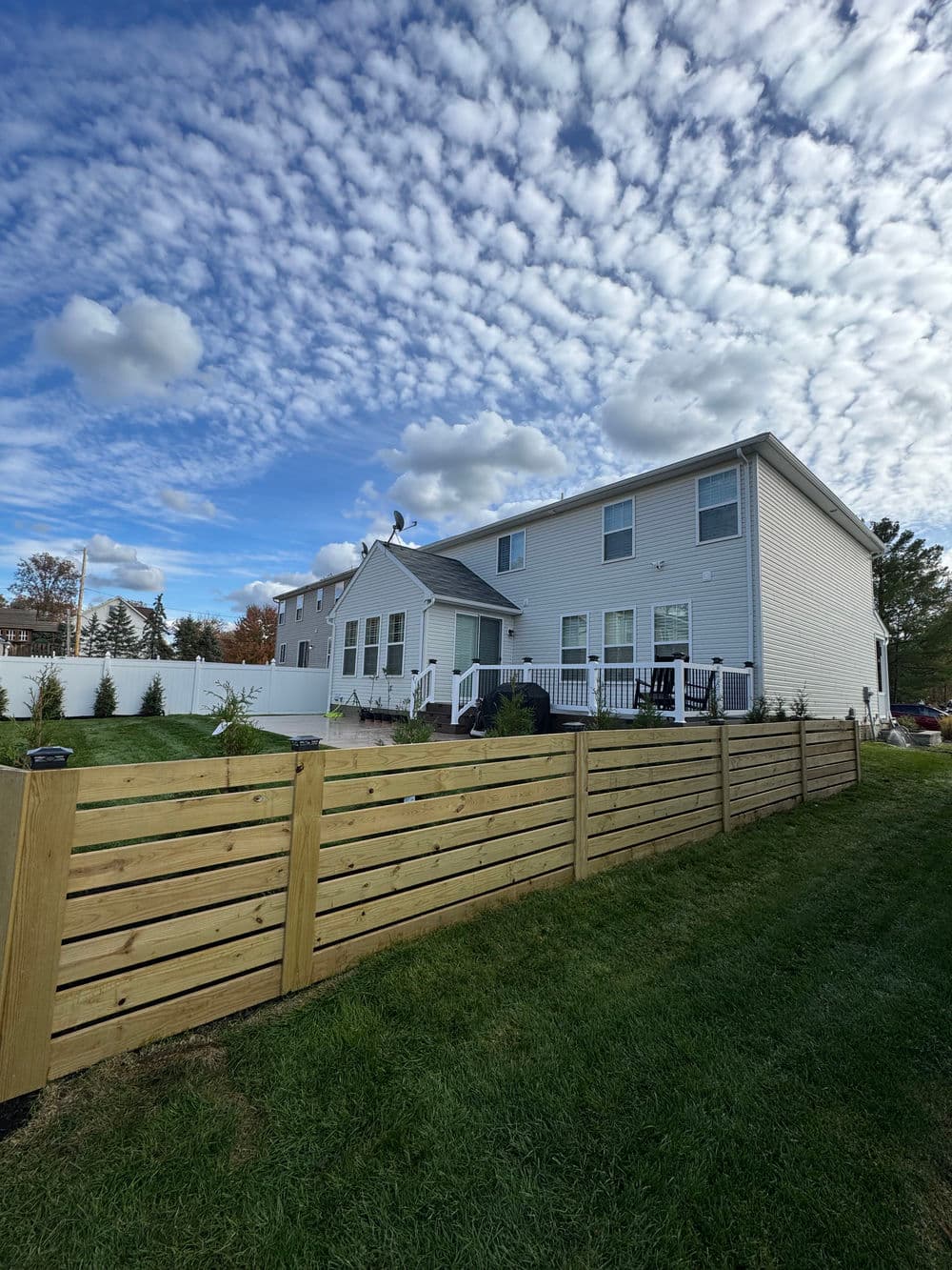 Modern two-story home with backyard, wooden fence, and cloudy sky. Ideal for family living.