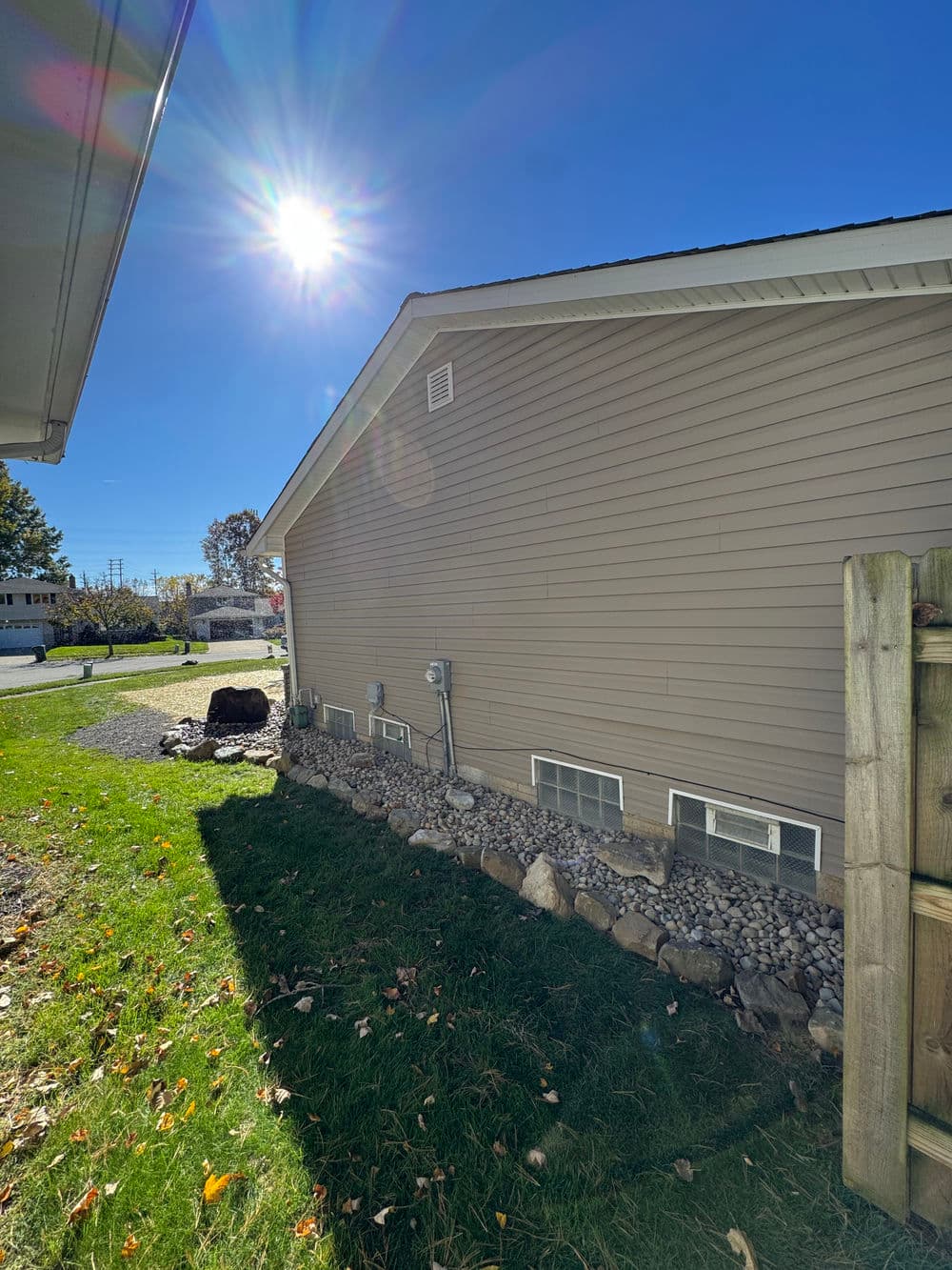 Side view of a beige house with sunny blue sky, grass, and rock landscaping.