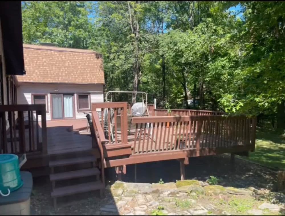 Spacious wooden deck surrounded by lush greenery, ideal for outdoor relaxation.