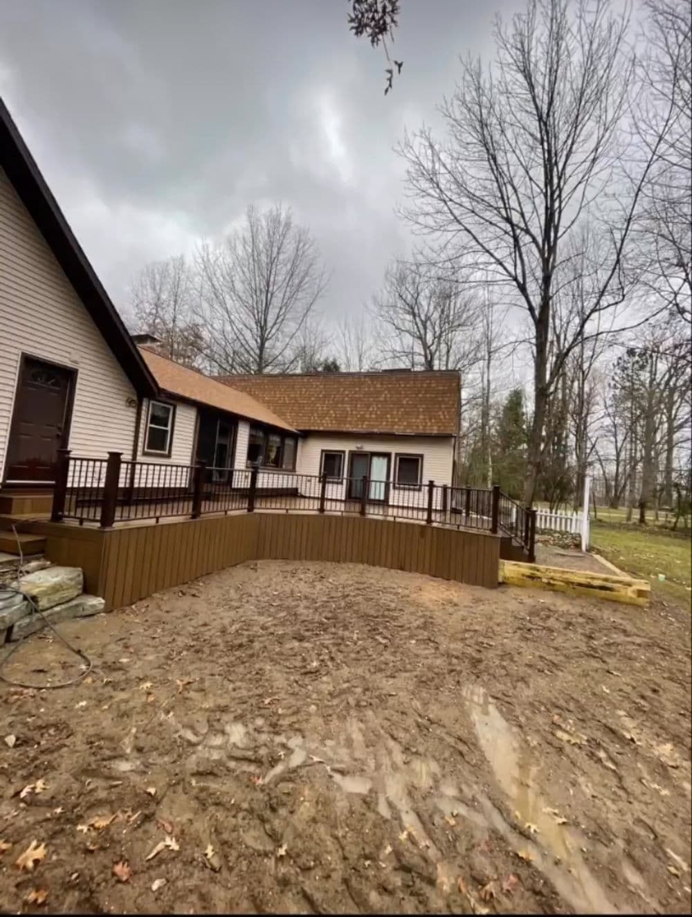 Newly built wooden deck attached to a house in a wooded area under cloudy skies.