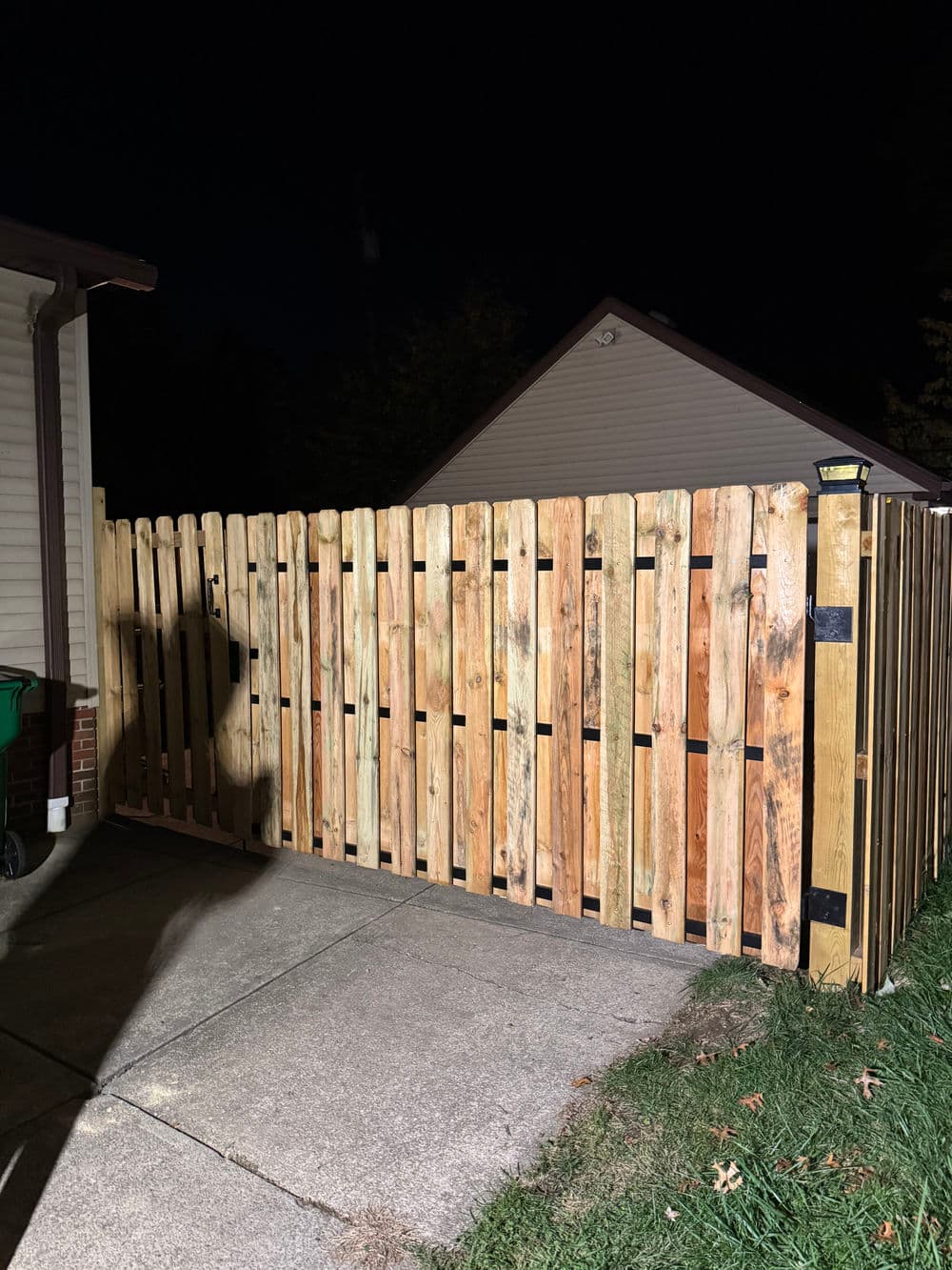 Wooden fence gate at night, showcasing vertical slats and a well-lit entrance.