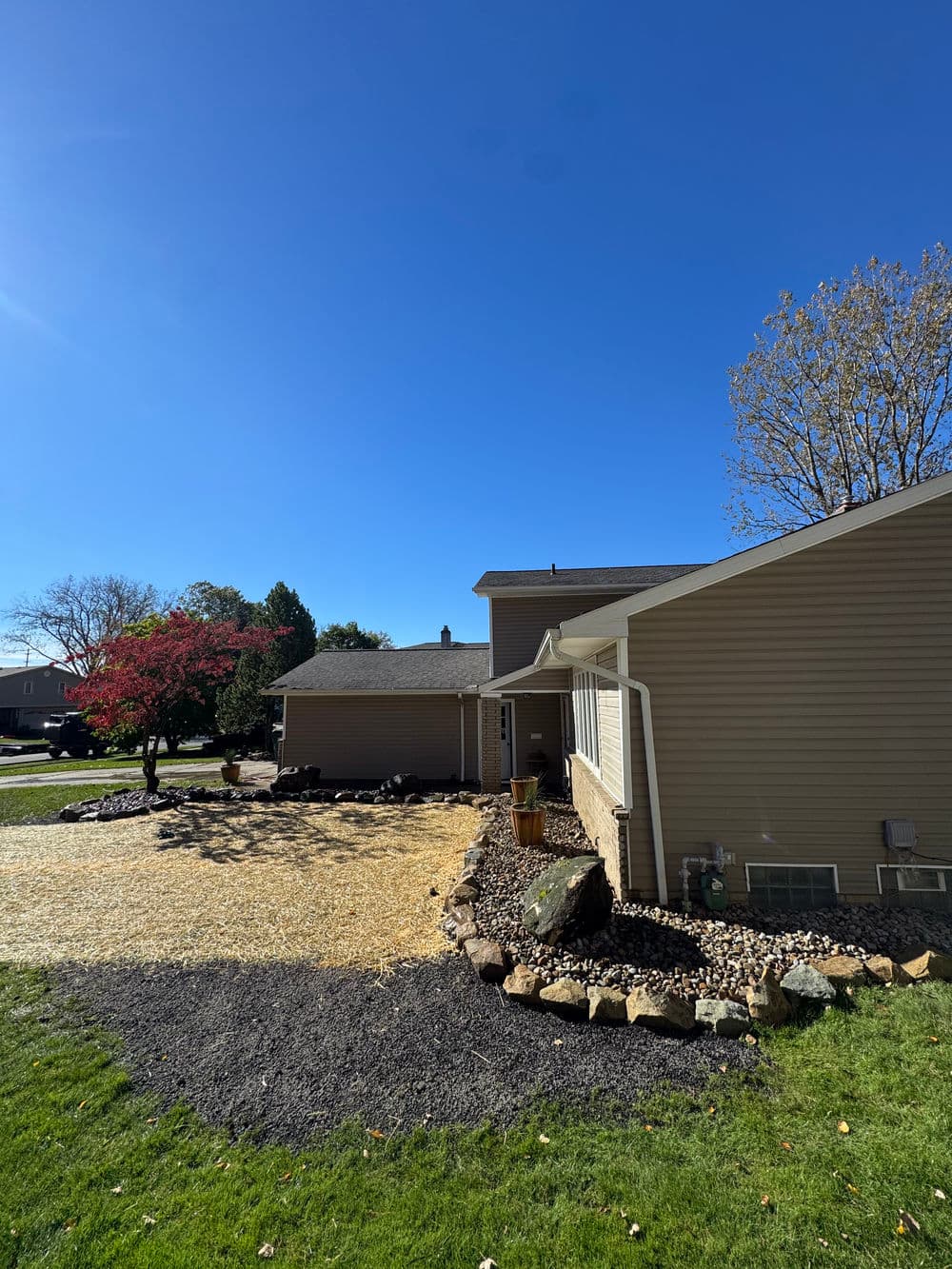 Side view of a modern house with landscaping, clear sky, and vibrant trees in autumn.