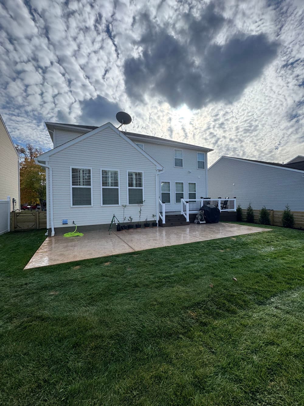 Two-story house with a backyard patio, grassy lawn, and cloudy sky in the background.