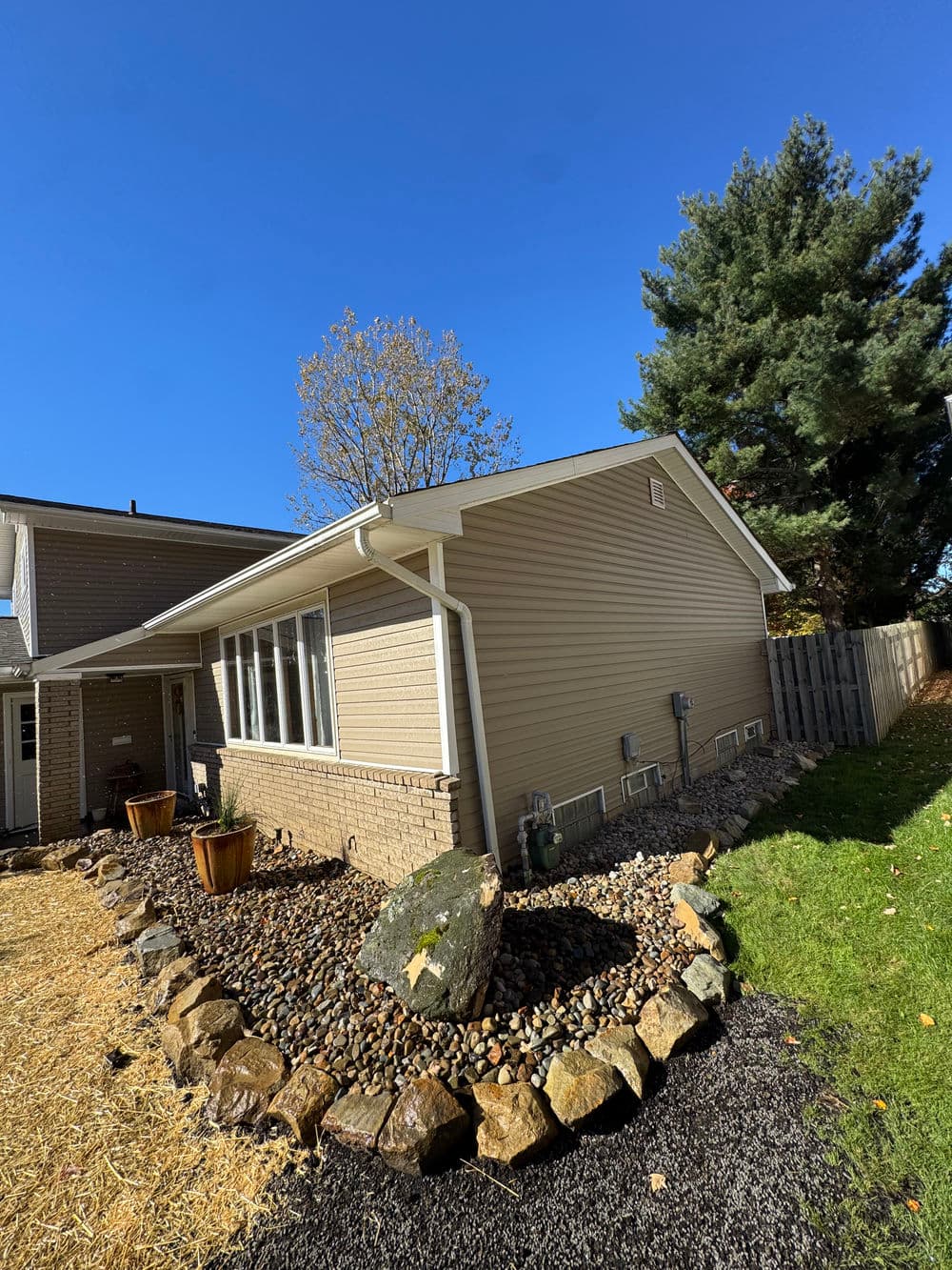 Side view of a beige house with a landscaped yard and clear blue sky.