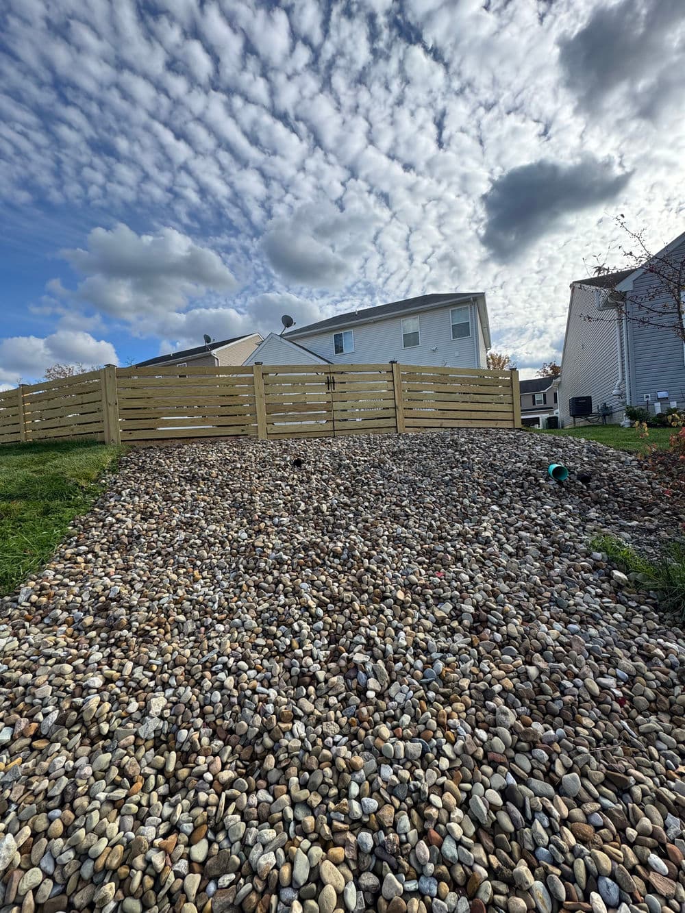Gravel yard with wooden fence and cloudy sky, showcasing suburban landscape.